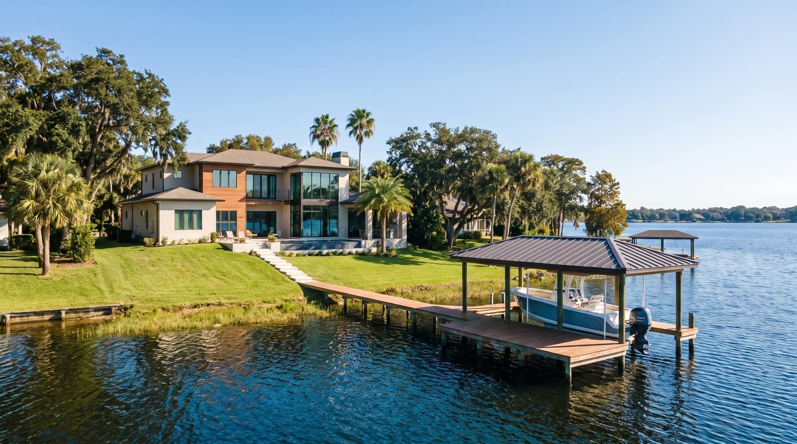 A modern Florida lakefront home on a gently sloping lawn above a large blue lake with a dock and boat lift
